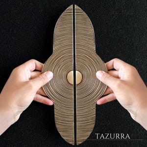 May include: Two brass-colored door handles with a unique design. Each handle is a half-oval shape with concentric circular grooves and a central circular accent. The handles are held together, with the word "TAZURRA" visible in the lower right corner.