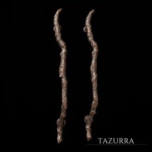 May include: Two vertical door handles with a dark bronze finish and a textured, organic surface that mimics the appearance of gnarled tree branches. Each handle features two circular mounting points and the text TAZURRA in the bottom corner.