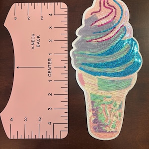 May include: A colorful sequined ice cream cone patch with pink, blue, and purple details. A pink ruler with the text "V-NECK BACK" and measurements in inches is next to the patch.