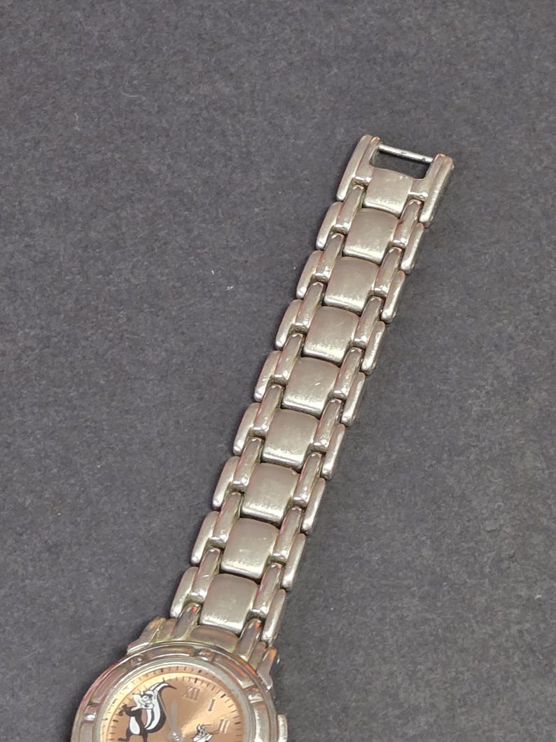 Pu&ograve; includere: Orologio da polso argentato con cinturino a maglie rettangolari. Il quadrante dell'orologio presenta un design di personaggi dei cartoni animati su sfondo marrone chiaro. Display analogico classico.