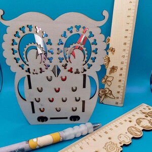 Peut inclure: Une décoration en bois en forme de hibou avec des détails découpés, accompagnée de deux règles en bois et d'un stylo. Une règle porte le nom "Marius". L'autre règle est graduée jusqu'à 20 pouces (50.8 cm).