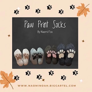 Pode incluir: Seis pares de meias com desenhos de pegadas de patas. As meias são em várias cores, incluindo cinza, preto e branco, com pegadas de patas em tons de marrom e rosa. O texto "Paw Print Socks By Naomi Fox" é exibido.