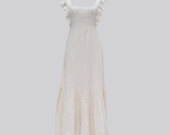 Puede incluir: Un vestido largo color crema con escote cuadrado y tirantes con volantes. El vestido presenta un corpiño ajustado y una falda escalonada, creando una silueta fluida. La tela parece ligera y texturizada, adecuada para climas cálidos.