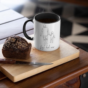 May include: A white coffee mug with a black handle and rim, featuring a line drawing of a parent and child with the text "Best dad ever." A slice of bread and a knife rest on a wooden cutting board.