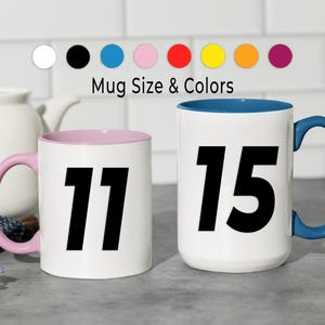 May include: Two white ceramic mugs with black numbers 11 and 15. One mug has a pink interior and handle, the other has a blue interior and handle. The text "Mug Size & Colors" is above the mugs, with color swatches.