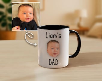 Op de afbeelding: Witte keramische mok met een zwarte binnenkant en handvat. De mok heeft een foto van een babygezicht, met de tekst "Liam's" boven de afbeelding en "DAD" eronder. Een kleinere afbeelding van de baby staat in de linkerbovenhoek.