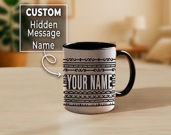 May include: A white ceramic mug with a black interior and handle. The mug features a black geometric pattern and the words "YOUR NAME" in a bold font. The mug is designed to be customised with a hidden message.