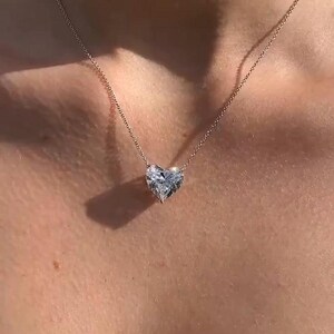 May include: A delicate gold necklace featuring a heart-shaped diamond pendant. The pendant is faceted, catching the light, and suspended from a thin chain. The necklace rests on a person's skin, highlighting the jewelry's design.