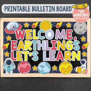 May include: A rectangular bulletin board with a wooden frame featuring a space-themed design. The black background displays colorful planets, stars, comets, a sun, a moon, and two astronauts. The text reads: WELCOME, EARTHLINGS, LET'S LEARN.