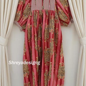 K&ouml;nnte beinhalten: Ein langes, rotes Kleid mit vertikalem Streifenmuster und Tigerprint. Das Kleid hat lange, puffige &Auml;rmel und ein gestreiftes Oberteil. Der Text "Shreyadesigng" ist unten links auf dem Kleid zu sehen.
