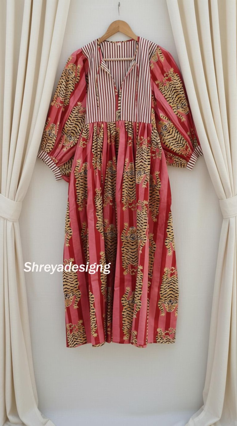 K&ouml;nnte beinhalten: Ein langes, rotes Kleid mit vertikalem Streifenmuster und Tigerprint. Das Kleid hat lange, puffige &Auml;rmel und ein gestreiftes Oberteil. Der Text "Shreyadesigng" ist unten links auf dem Kleid zu sehen.