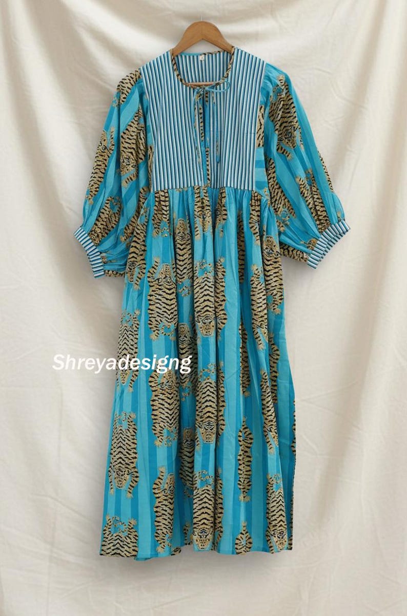 K&ouml;nnte beinhalten: Ein langes, flie&szlig;endes blaues Kleid mit Tigerstreifenmuster. Das Kleid hat ein gestreiftes Oberteil und &Auml;rmel mit einem Schn&uuml;rhalsausschnitt. Der Text "Shreyadesigng" ist auf das Kleid gedruckt.