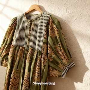 K&ouml;nnte beinhalten: Ein gr&uuml;nes Kleid mit Tigerprint und gestreiftem Oberteil. Das Kleid hat lange &Auml;rmel und eine Kordel am Ausschnitt. Der Text "Shreyadesigng" ist unten sichtbar.