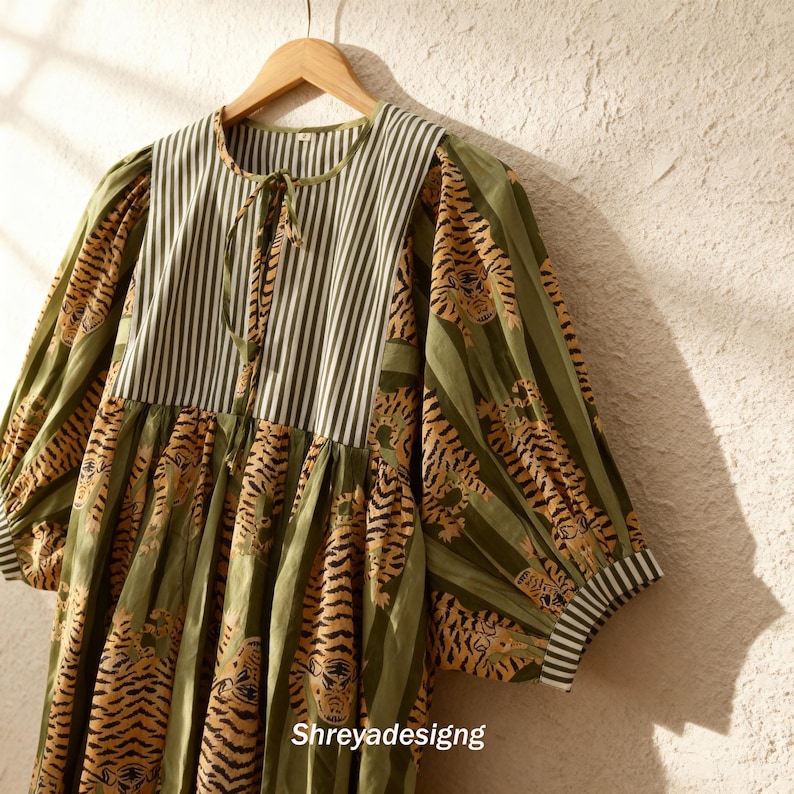 K&ouml;nnte beinhalten: Ein gr&uuml;nes Kleid mit Tigerprint und gestreiftem Oberteil. Das Kleid hat lange &Auml;rmel und eine Kordel am Ausschnitt. Der Text "Shreyadesigng" ist unten sichtbar.