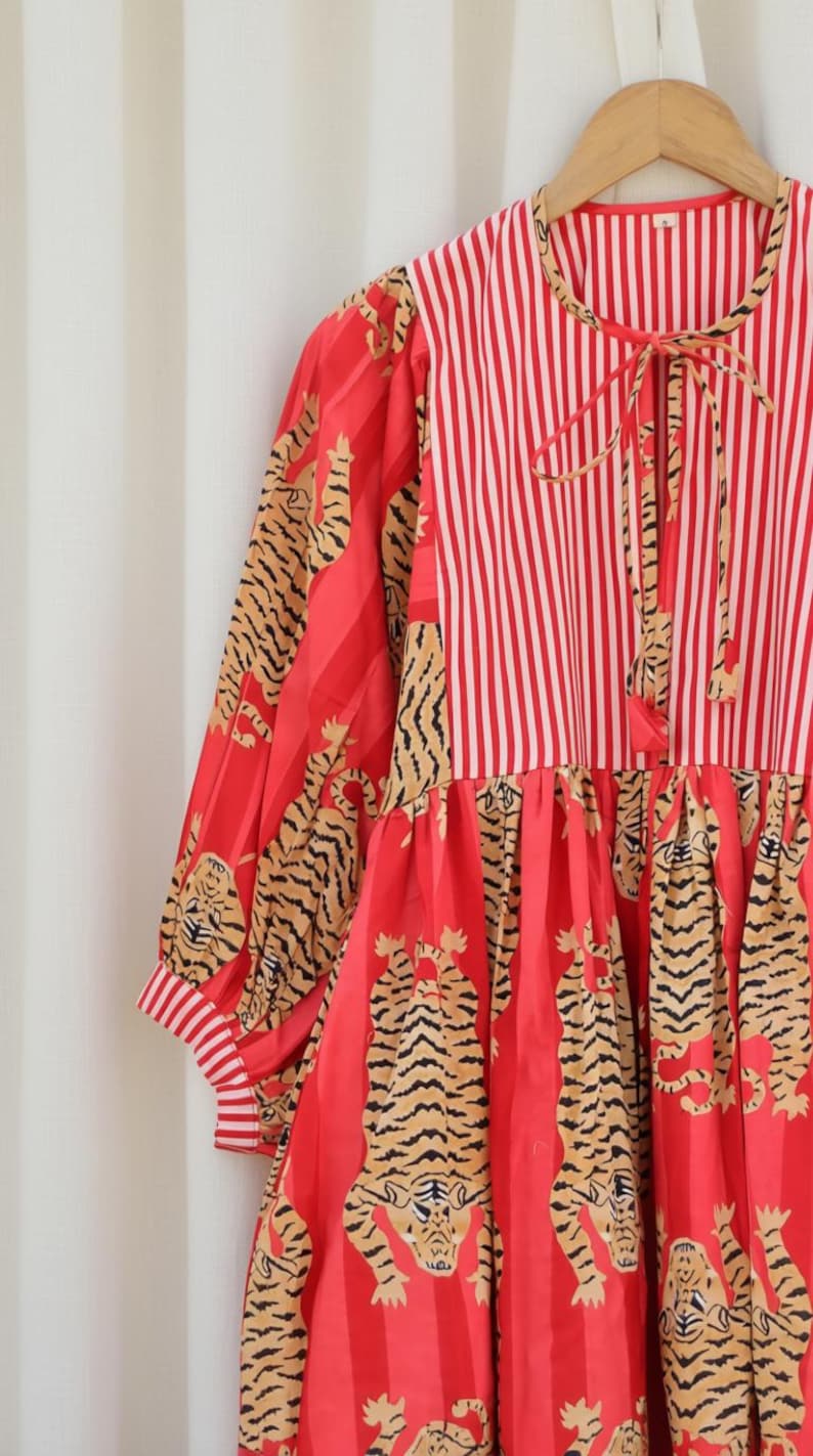 K&ouml;nnte beinhalten: Rot-wei&szlig; gestreiftes Kleid mit Tigerprint. Das Kleid hat lange &Auml;rmel mit gestreiften Manschetten und einen Bindekragen. Der Rock hat ein auff&auml;lliges Tigermuster. Das Kleid h&auml;ngt an einem Holzkleiderb&uuml;gel.
