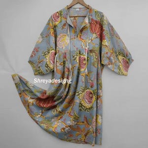 Puede incluir: Vestido azul claro con estampado floral, corte holgado y mangas de codo. Cuello en V con cordón. Estampado floral colorido en tonos rosa, amarillo y marrón. El texto "Shreyadesigng" es visible.