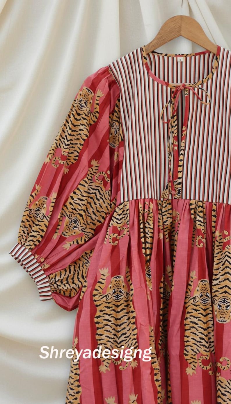 K&ouml;nnte beinhalten: Kleid mit Streifen- und Tigerdruckmustern. Das Oberteil ist rot-wei&szlig; gestreift, mit einem Schn&uuml;rhalsausschnitt. Die &Auml;rmel und der Rock haben einen Tigerdruck auf rotem Hintergrund. Der Text "Shreyadesigng" ist sichtbar.