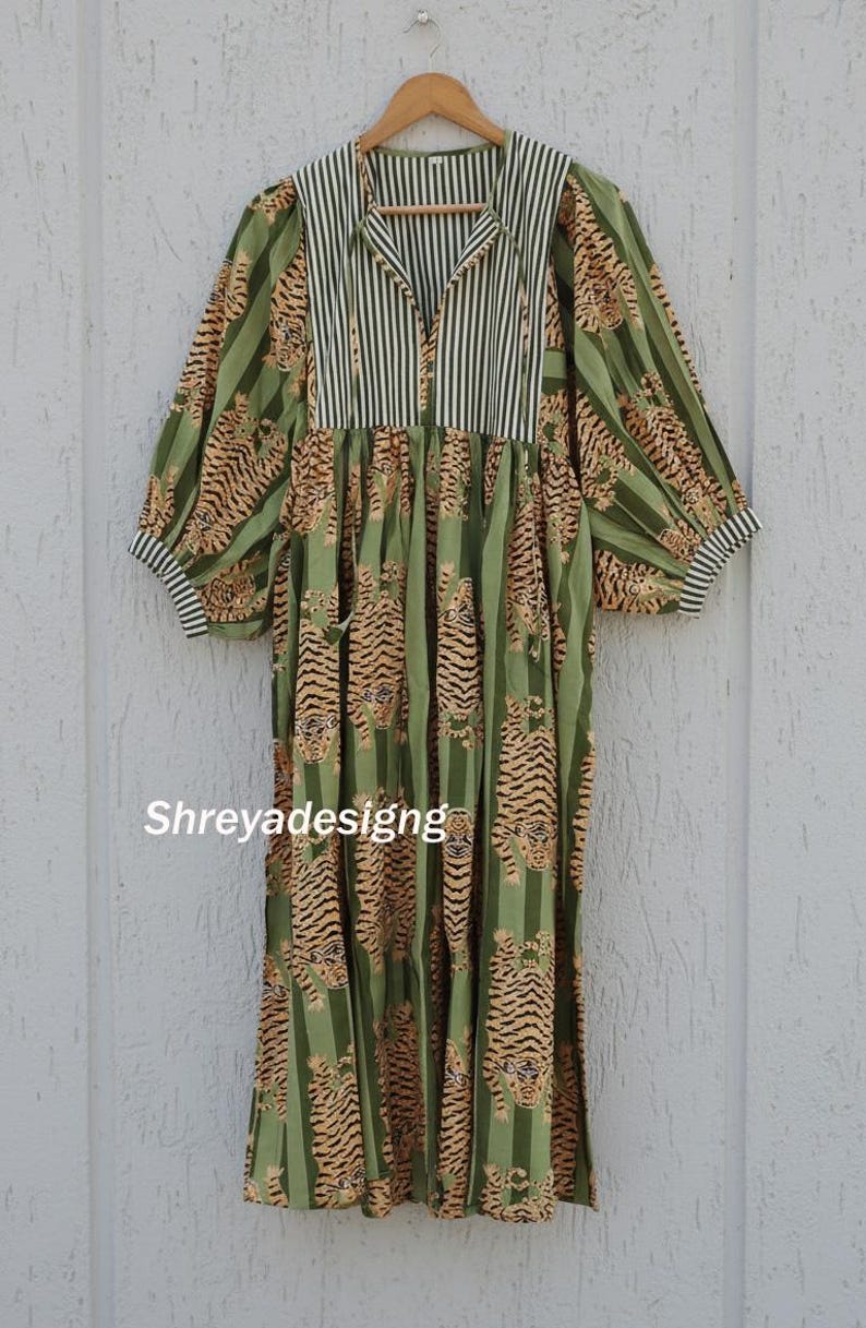 K&ouml;nnte beinhalten: Ein langes, gr&uuml;nes Kleid mit Tigerprint und vertikalen Streifen. Das Kleid hat einen Kragen mit schwarz-wei&szlig;en Streifen, lange &Auml;rmel und den Text "Shreyadesigng".