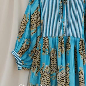 K&ouml;nnte beinhalten: Ein blaues Kleid mit Tigerprint und vertikalen Streifen. Das Kleid hat lange &Auml;rmel mit gestreiften Manschetten und ein gestreiftes Oberteil. Der Tigerprint ist in Braun- und Schwarzt&ouml;nen gehalten. Der Text "Shreyadesigng" ist sichtbar.