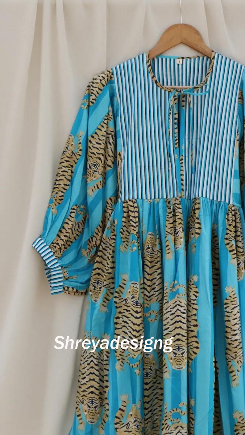 K&ouml;nnte beinhalten: Ein blaues Kleid mit Tigerprint und vertikalen Streifen. Das Kleid hat lange &Auml;rmel mit gestreiften Manschetten und ein gestreiftes Oberteil. Der Tigerprint ist in Braun- und Schwarzt&ouml;nen gehalten. Der Text "Shreyadesigng" ist sichtbar.