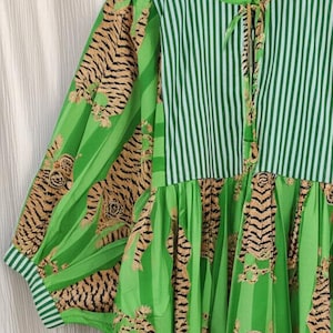 K&ouml;nnte beinhalten: Ein gr&uuml;nes Kleid mit gestreiftem Oberteil und &Auml;rmeln mit Tigerstreifenmuster. Das Kleid hat einen runden Ausschnitt mit Bindeband und der Text "Shreyadesigng" ist sichtbar.