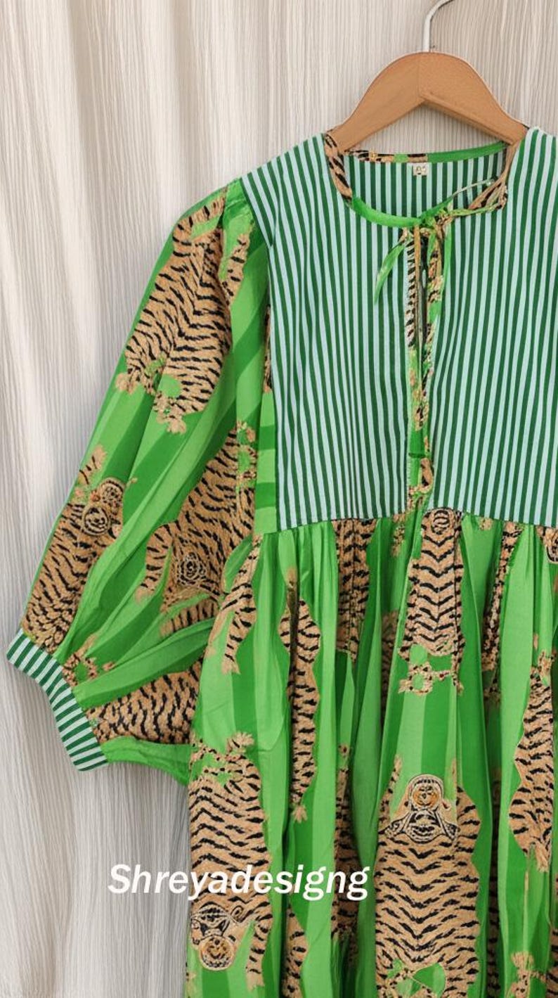 K&ouml;nnte beinhalten: Ein gr&uuml;nes Kleid mit gestreiftem Oberteil und &Auml;rmeln mit Tigerstreifenmuster. Das Kleid hat einen runden Ausschnitt mit Bindeband und der Text "Shreyadesigng" ist sichtbar.