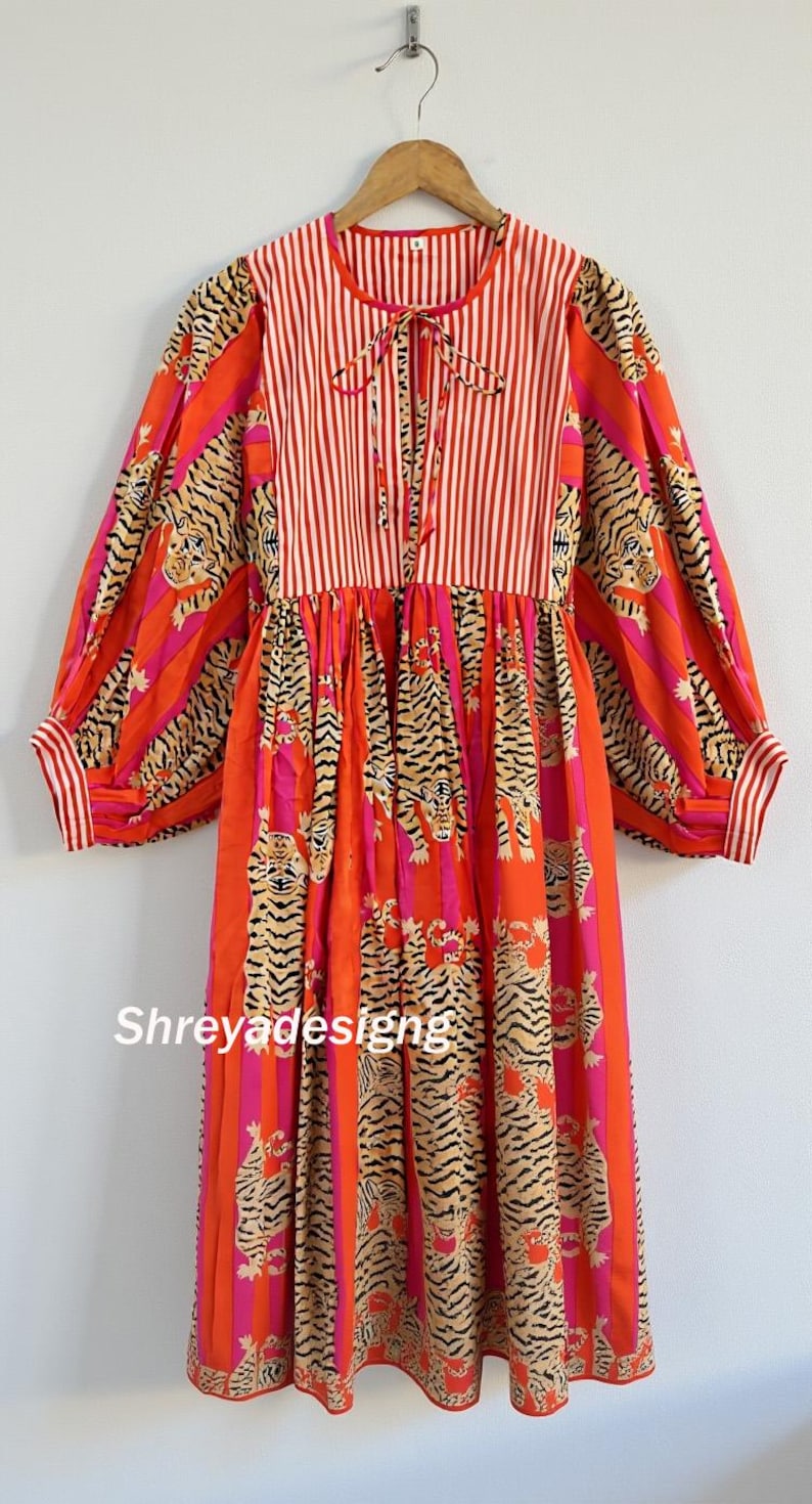 K&ouml;nnte beinhalten: Langes Kleid mit Tigerstreifenmuster in Orange, Pink und Schwarz. Das Oberteil hat rot-wei&szlig;e vertikale Streifen und einen Bindekragen. Lange &Auml;rmel mit Manschetten. Der Name "Shreyadesigng" ist sichtbar.