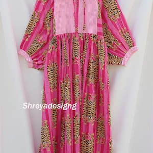 K&ouml;nnte beinhalten: Ein rosa Kleid mit Tigerprint und vertikalen Streifen. Das Kleid hat lange &Auml;rmel mit gestreiften Manschetten und ein gestreiftes Oberteil mit Bindeband. Der Text "Shreyadesigng" ist auf dem Kleid zu sehen.