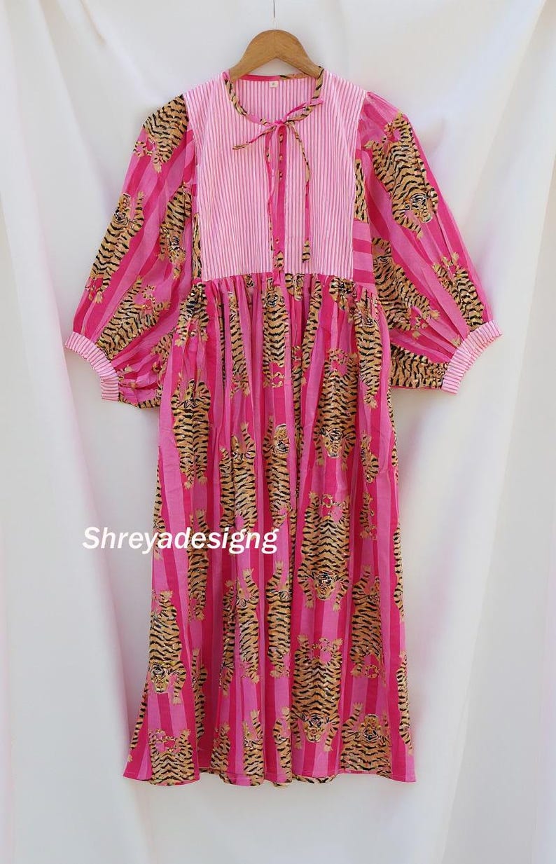 K&ouml;nnte beinhalten: Ein rosa Kleid mit Tigerprint und vertikalen Streifen. Das Kleid hat lange &Auml;rmel mit gestreiften Manschetten und ein gestreiftes Oberteil mit Bindeband. Der Text "Shreyadesigng" ist auf dem Kleid zu sehen.