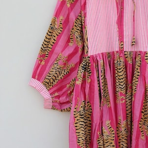 K&ouml;nnte beinhalten: Rosa Kleid mit gestreiftem Oberteil und &Auml;rmeln mit Tigerprint. Das Kleid hat ein Bindeband am Hals und der Text "Shreyadesigng" ist auf der Vorderseite sichtbar.