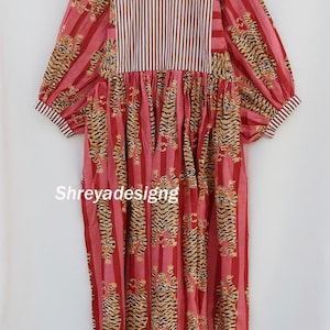 K&ouml;nnte beinhalten: Ein rotes und rosa Kleid mit Tigerprint und gestreiftem Oberteil. Das Kleid hat ein vertikales Streifenmuster mit Tigerillustrationen. Die &Auml;rmel sind lang und puffig, und das Kleid h&auml;ngt an einem Holzkleiderb&uuml;gel.