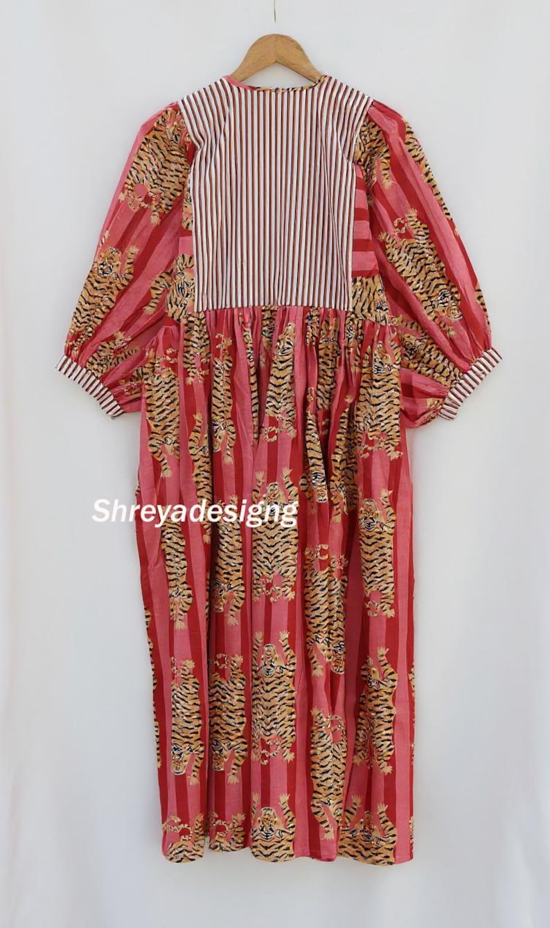 K&ouml;nnte beinhalten: Ein rotes und rosa Kleid mit Tigerprint und gestreiftem Oberteil. Das Kleid hat ein vertikales Streifenmuster mit Tigerillustrationen. Die &Auml;rmel sind lang und puffig, und das Kleid h&auml;ngt an einem Holzkleiderb&uuml;gel.