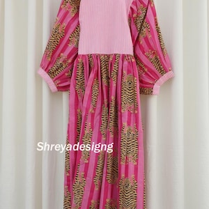 K&ouml;nnte beinhalten: Ein rosa Kleid mit vertikalen Streifen und Tigerprint. Das Kleid hat lange &Auml;rmel und einen runden Ausschnitt. Der obere Teil des Kleides ist einfarbig rosa mit vertikalen Streifen. Das Kleid h&auml;ngt an einem Holzb&uuml;gel. Der Text "Shreyadesigng" ist sichtbar.