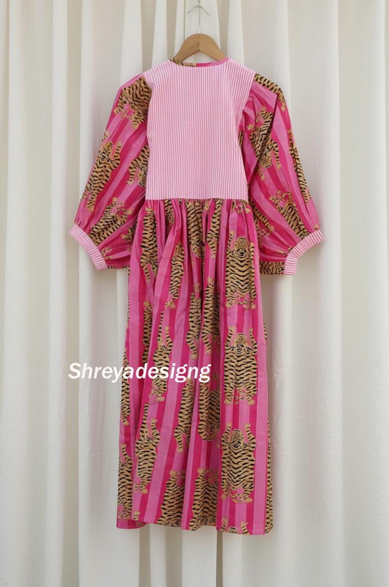 K&ouml;nnte beinhalten: Ein rosa Kleid mit vertikalen Streifen und Tigerprint. Das Kleid hat lange &Auml;rmel und einen runden Ausschnitt. Der obere Teil des Kleides ist einfarbig rosa mit vertikalen Streifen. Das Kleid h&auml;ngt an einem Holzb&uuml;gel. Der Text "Shreyadesigng" ist sichtbar.