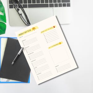 May include: A cream-coloured weekly planner with the text "WEEKLY SHIT TO DO" and "URGENT SHIT THIS WEEK". The planner includes sections for each day of the week, with space for notes. A pen, glasses, and a laptop are also visible.