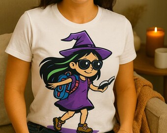 Puede incluir: Camiseta blanca con una niña bruja de dibujos animados con un vestido, sombrero y gafas de sol moradas, que lleva una mochila y un libro. La ilustración tiene cabello negro con reflejos verdes. La bruja camina sobre un camino morado.