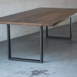 May include: A long, dark brown wooden table with black metal legs. The table is sitting on a concrete floor.