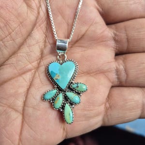 May include: A silver necklace with a turquoise heart-shaped pendant and turquoise teardrop-shaped accents. The pendant is suspended from a delicate silver chain. The turquoise stones have brown and yellow markings.