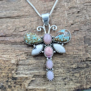 May include: A silver dragonfly pendant necklace. The dragonfly design features turquoise, pink, and white gemstones set in a silver frame. The pendant hangs from a delicate silver chain, creating a unique and eye-catching piece of jewelry.
