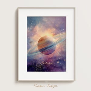 May include: Watercolor painting of Saturn with its rings, set against a backdrop of a nebula in shades of purple, blue, and orange. The word "Saturn" is written in a cursive font. The artwork is framed in a silver frame.