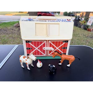 Op de afbeelding: Een vintage Fisher-Price Family Farm speelset. De witte schuur heeft rode deuren met een X-ontwerp. Inclusief een koe, paard, kip en varken. De speelset heeft de tekst "Fisher-Price Family Farm" erop.