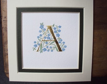 Initial letter in 23c gold leaf with forget me not flower letter.