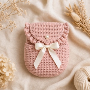 Peut inclure: Un sac rose en crochet fait à la main, avec un rabat à volants et une fermeture à bouton perlé. Le sac est orné d'un nœud en satin crème et d'un point texturé. Ce petit sac élégant est parfait pour transporter de petits objets.