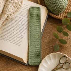 Peut inclure: Un marque-page rectangulaire vert sauge réalisé avec un motif de points au crochet dense et uniforme. Le marque-page présente une forme plate et allongée avec des coins arrondis et une surface texturée cohérente sur toute sa longueur.