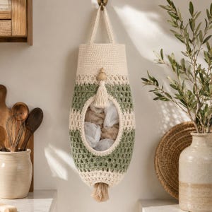 Peut inclure: Un porte-sacs en plastique crocheté crème et vert avec une perle en bois et une gland. Le support est de forme ovale avec une grande ouverture au centre et un trou de distribution en bas. Il est suspendu à un crochet en laiton.