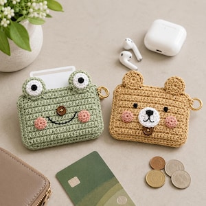 Peut inclure: Deux étuis en crochet, l'un vert en forme de grenouille et l'autre beige en forme d'ours, avec des anneaux dorés. L'étui grenouille a de grands yeux bordés de blanc et des joues roses. L'étui ours a un museau blanc et des joues roses. Les deux étuis ont une fermeture à bouton.