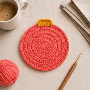 Peut inclure: Un dessous de verre rond au crochet de couleur corail, doté d'une petite languette rectangulaire jaune moutarde sur le dessus. Le dessous de verre est réalisé avec un point circulaire dense, créant une surface plate et texturée.