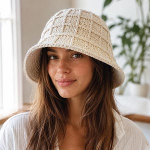 Peut inclure: Chapeau seau en crochet de couleur crème avec un motif carré. Le chapeau a un large bord et une couronne arrondie. Le chapeau est fait d'un fil doux et texturé. Un accessoire élégant.