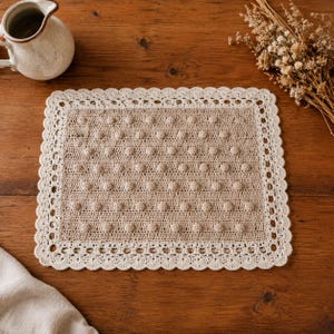 Peut inclure: Nappe rectangulaire en crochet beige avec un motif à pois et une bordure festonnée blanc cassé. Un petit pichet en céramique blanc cassé est dans le coin supérieur gauche, et des fleurs séchées sont dans le coin supérieur droit.