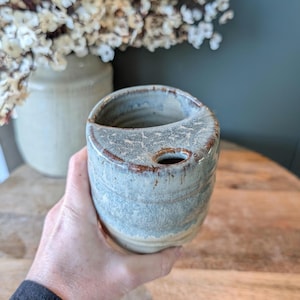 May include: A white ceramic mug with a black handle and the text "But First, Coffee" in a black, handwritten-style font. The mug is on a white surface.
